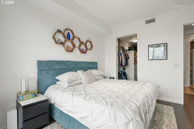 bedroom with baseboards, visible vents, wood finished floors, a walk in closet, and a closet