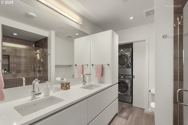 full bath featuring wood finished floors, a stall shower, a sink, and stacked washer and clothes dryer