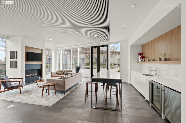 living room featuring beverage cooler, a wall of windows, indoor wet bar, and a glass covered fireplace