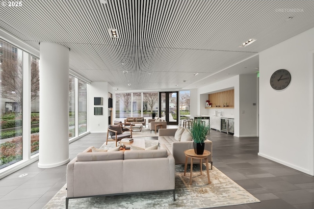 living room featuring expansive windows, ornate columns, indoor bar, and baseboards