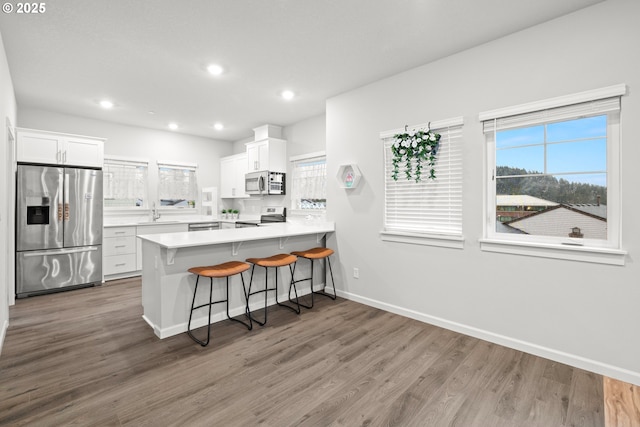 kitchen featuring hardwood / wood-style floors, white cabinets, a kitchen breakfast bar, appliances with stainless steel finishes, and kitchen peninsula