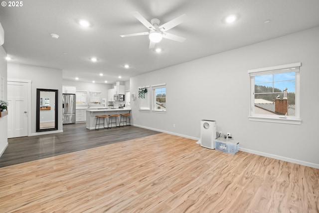 unfurnished living room with ceiling fan, a wealth of natural light, and light hardwood / wood-style flooring