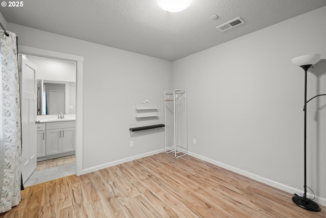 unfurnished room with a textured ceiling, light hardwood / wood-style flooring, and sink