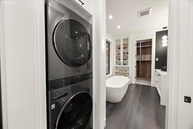 clothes washing area featuring dark tile patterned flooring and stacked washer / drying machine