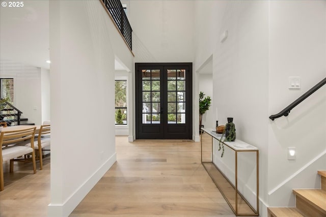 foyer with a towering ceiling, light hardwood / wood-style floors, and french doors