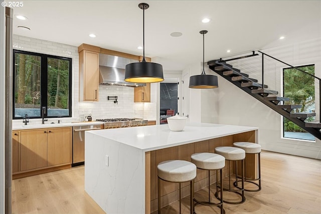 kitchen featuring appliances with stainless steel finishes, a center island, decorative light fixtures, wall chimney exhaust hood, and sink