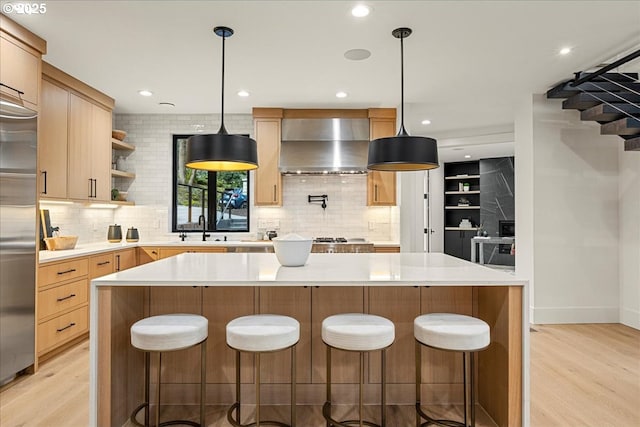 kitchen featuring light brown cabinets, light hardwood / wood-style flooring, wall chimney exhaust hood, and hanging light fixtures