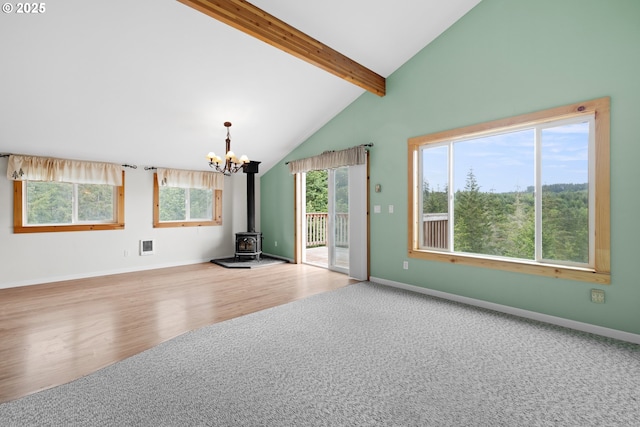 unfurnished living room with a chandelier, beamed ceiling, a wood stove, wood finished floors, and carpet floors