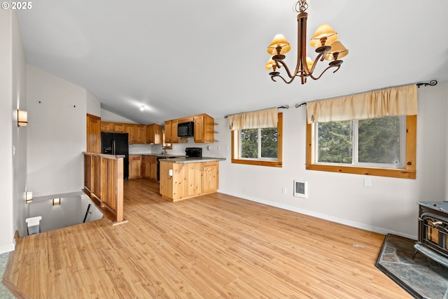kitchen with black appliances, a wood stove, light wood-style flooring, vaulted ceiling, and a chandelier
