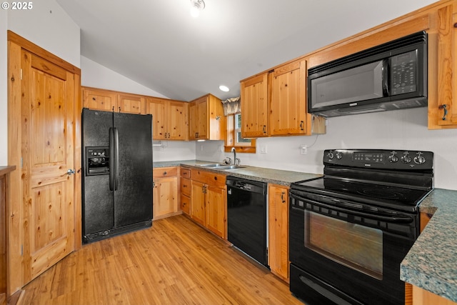 kitchen featuring black appliances, a sink, vaulted ceiling, light wood-type flooring, and dark countertops