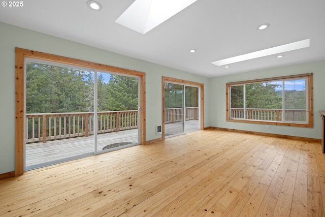 empty room featuring a skylight, wood-type flooring, recessed lighting, and baseboards