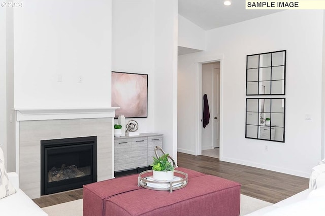 living area with wood finished floors, baseboards, a tiled fireplace, and recessed lighting