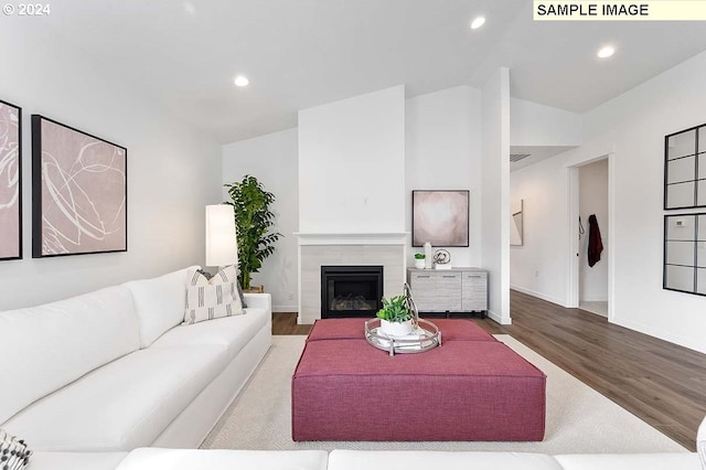 living room with wood finished floors, vaulted ceiling, a tiled fireplace, recessed lighting, and baseboards