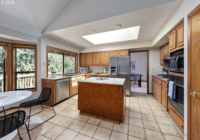 1929 SW Broadleaf Dr, Portland, OR 97219 - kitchen with appliances with stainless steel finishes, tile countertops, a skylight, a center island, and brown cabinets