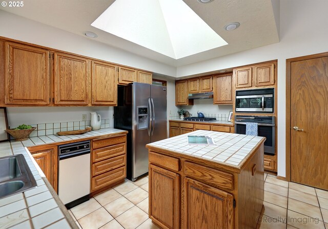 1929 SW Broadleaf Dr, Portland, OR 97219 - kitchen featuring stainless steel appliances, tile counters, under cabinet range hood, a skylight, and light tile patterned flooring