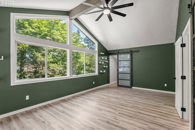 unfurnished room featuring wood finished floors, beamed ceiling, baseboards, ceiling fan, and a barn door
