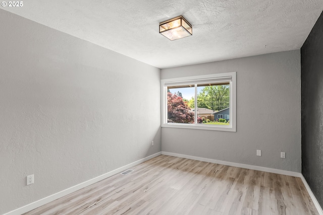 unfurnished room featuring baseboards, a textured ceiling, visible vents, and wood finished floors