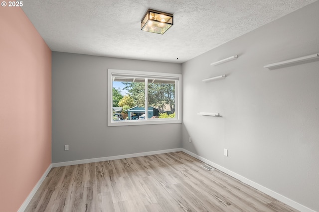 spare room featuring visible vents, baseboards, a textured ceiling, and wood finished floors