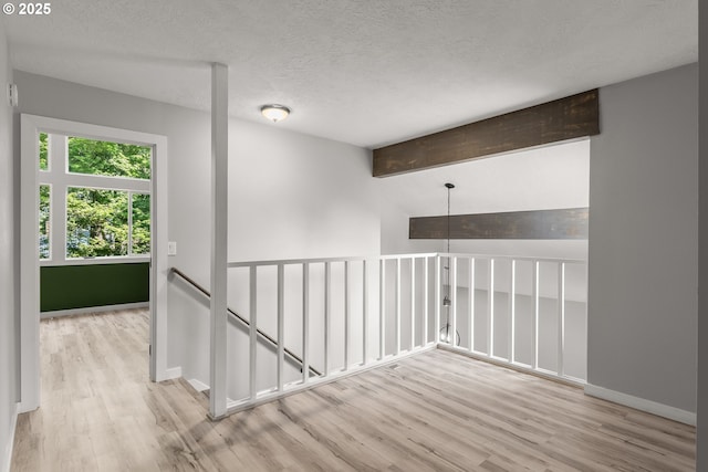 interior space featuring baseboards, a textured ceiling, wood finished floors, and beamed ceiling
