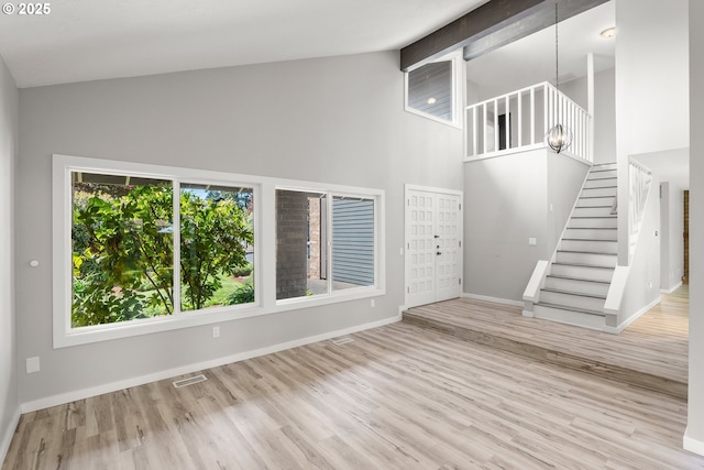 unfurnished living room featuring visible vents, wood finished floors, baseboards, high vaulted ceiling, and stairway