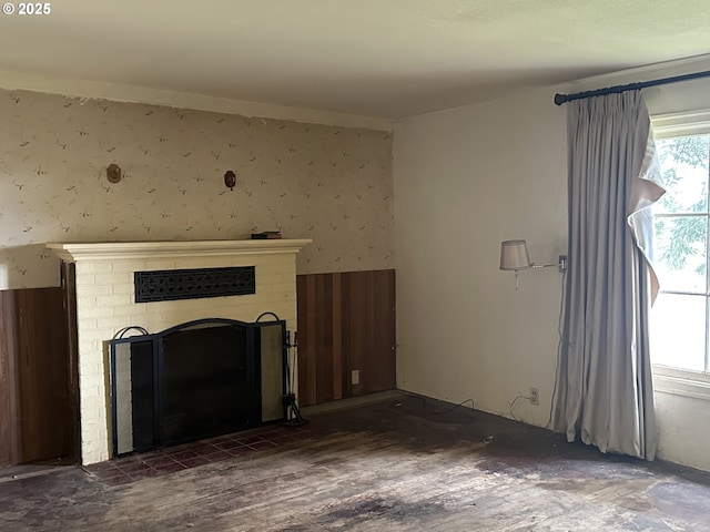 unfurnished living room featuring a brick fireplace, wallpapered walls, and wood finished floors