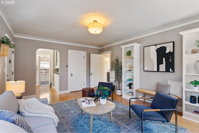 living room with arched walkways, light wood-style floors, ornamental molding, and baseboards
