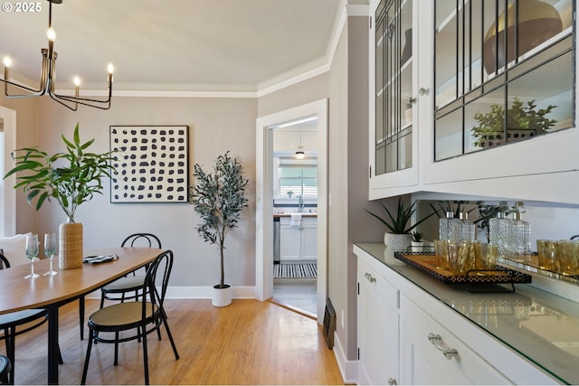 dining room with light wood-style flooring, a chandelier, baseboards, and crown molding