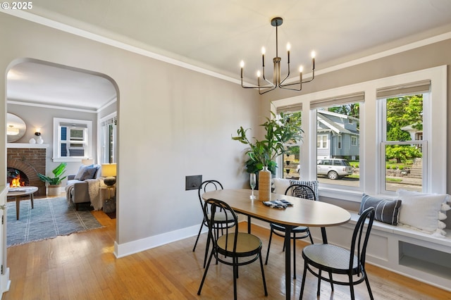 dining room featuring ornamental molding, arched walkways, light wood-style floors, a brick fireplace, and a chandelier