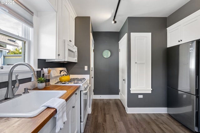 kitchen with white appliances, butcher block countertops, a sink, and white cabinets