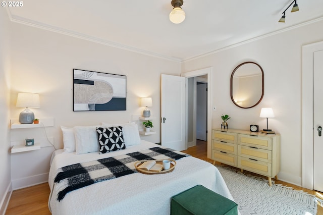 bedroom featuring crown molding, light wood finished floors, baseboards, and track lighting
