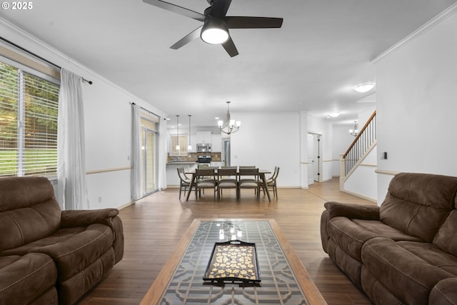 living room with ceiling fan with notable chandelier, ornamental molding, and light hardwood / wood-style flooring