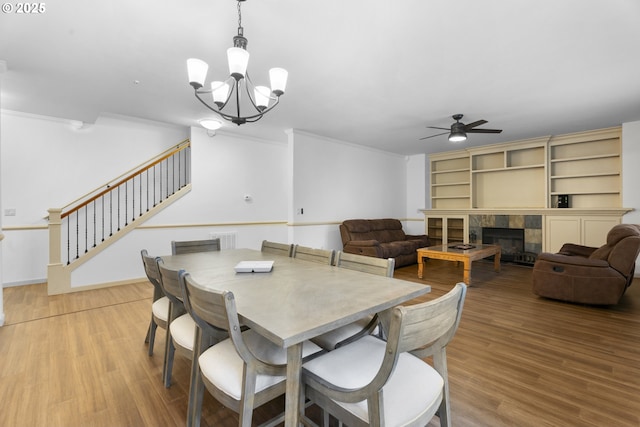 dining area with a tile fireplace, ceiling fan with notable chandelier, hardwood / wood-style flooring, and crown molding