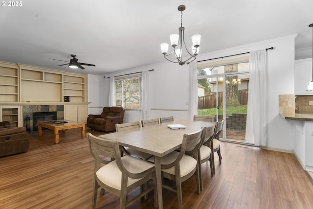 dining area featuring ceiling fan with notable chandelier, light hardwood / wood-style floors, crown molding, and a tiled fireplace