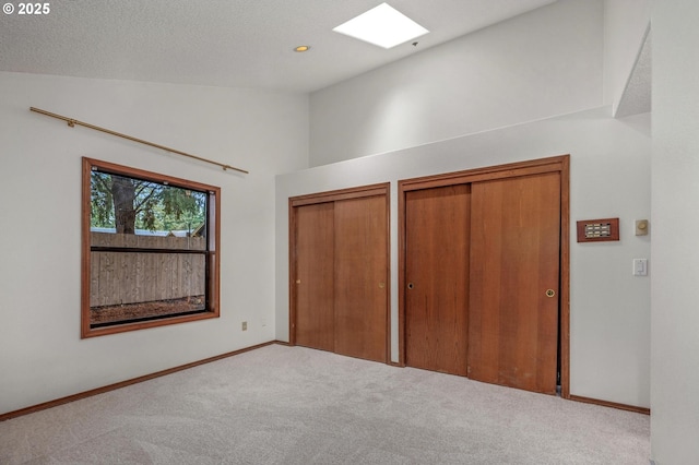 unfurnished bedroom featuring multiple closets, light colored carpet, and vaulted ceiling with skylight