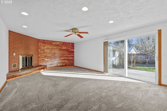 unfurnished living room featuring a brick fireplace, carpet floors, a textured ceiling, and wooden walls