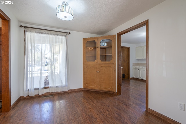 unfurnished dining area featuring lofted ceiling, dark hardwood / wood-style floors, and a textured ceiling