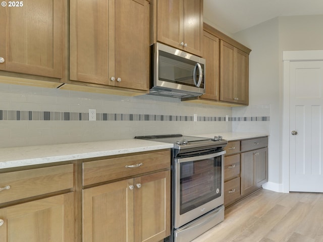 kitchen featuring backsplash, appliances with stainless steel finishes, light stone counters, and light wood finished floors