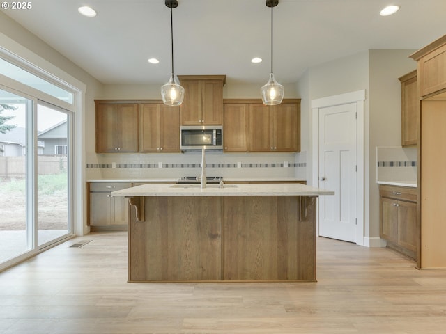 kitchen with decorative backsplash, decorative light fixtures, light hardwood / wood-style flooring, and a kitchen island with sink