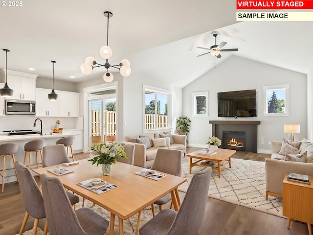 dining space with a glass covered fireplace, baseboards, wood finished floors, lofted ceiling, and ceiling fan