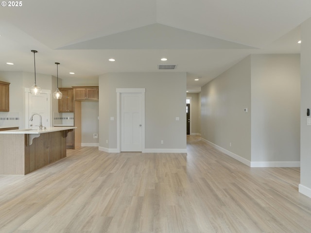 kitchen with pendant lighting, light hardwood / wood-style flooring, vaulted ceiling, and a kitchen island with sink