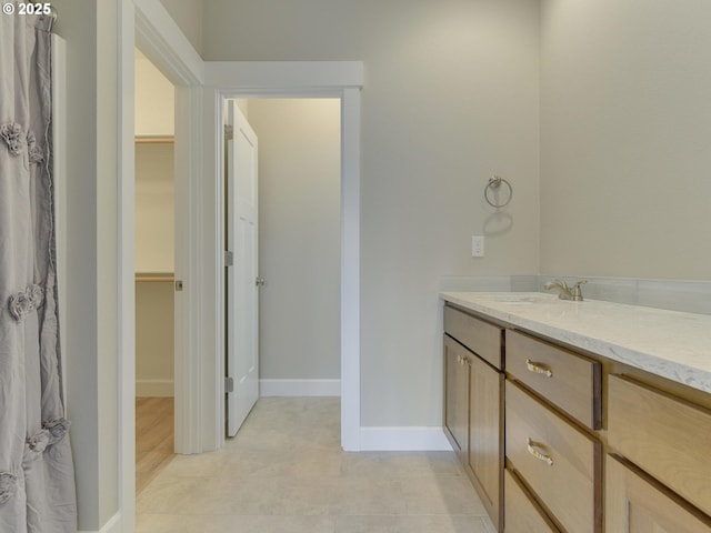 full bathroom with baseboards, a walk in closet, and vanity