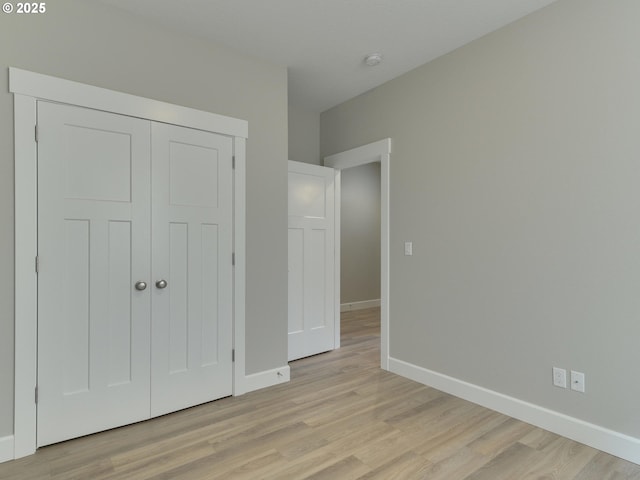 unfurnished bedroom with a closet, baseboards, and light wood-type flooring