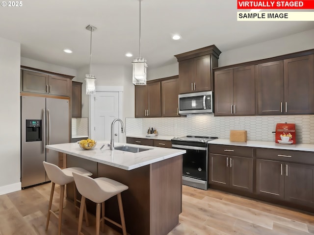 kitchen with appliances with stainless steel finishes, light wood finished floors, a sink, and dark brown cabinets