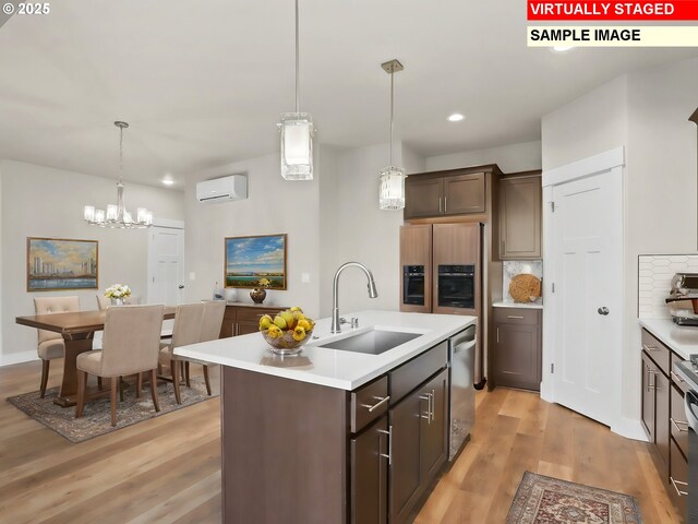 kitchen with light wood-style floors, stainless steel dishwasher, light countertops, a sink, and an AC wall unit