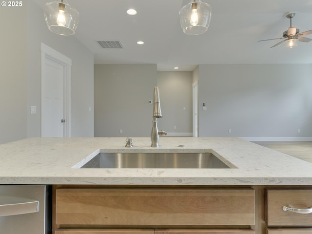 kitchen with light stone counters, a sink, a ceiling fan, and visible vents