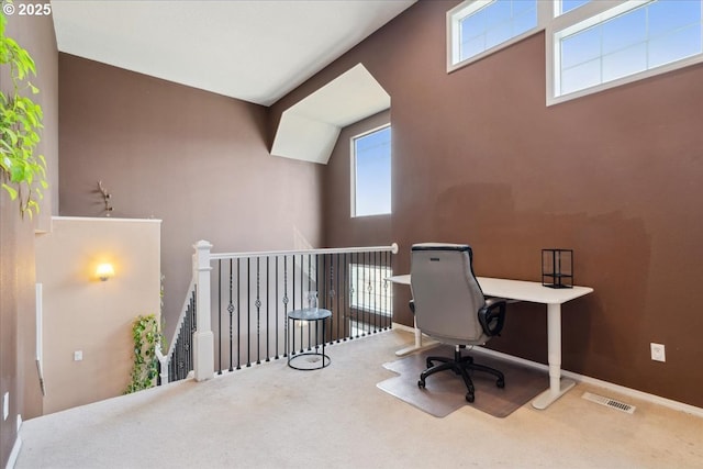 carpeted office space featuring baseboards, visible vents, and a towering ceiling