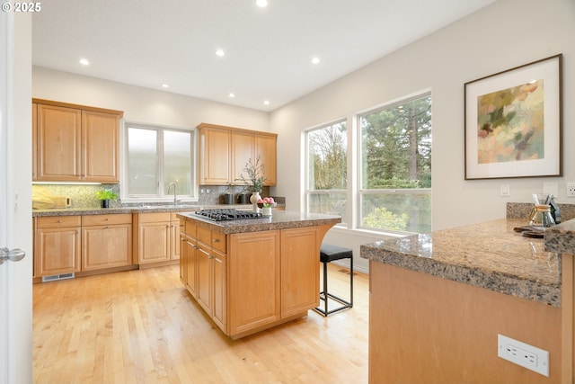 kitchen featuring stainless steel gas cooktop, a center island, light hardwood / wood-style flooring, a kitchen breakfast bar, and decorative backsplash