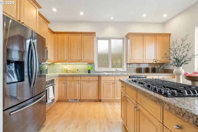 kitchen featuring stainless steel appliances, sink, light hardwood / wood-style flooring, and backsplash