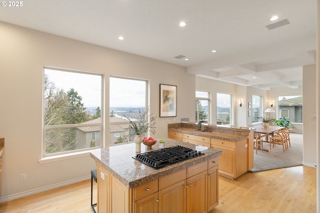 kitchen with a breakfast bar, black gas cooktop, a center island, light brown cabinets, and light wood-type flooring