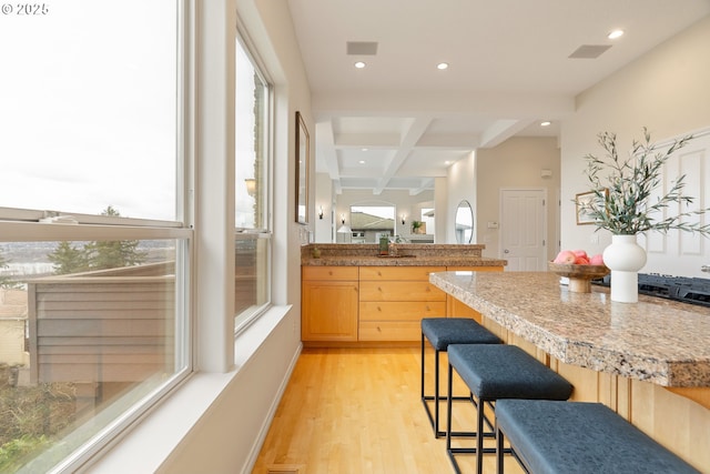 kitchen featuring a kitchen bar, coffered ceiling, light hardwood / wood-style flooring, light brown cabinets, and beam ceiling